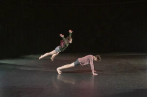 A dancer jumps over another dancer.